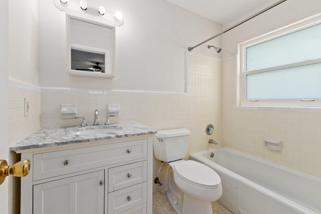 full bathroom featuring tiled shower / bath, vanity, toilet, and tile walls