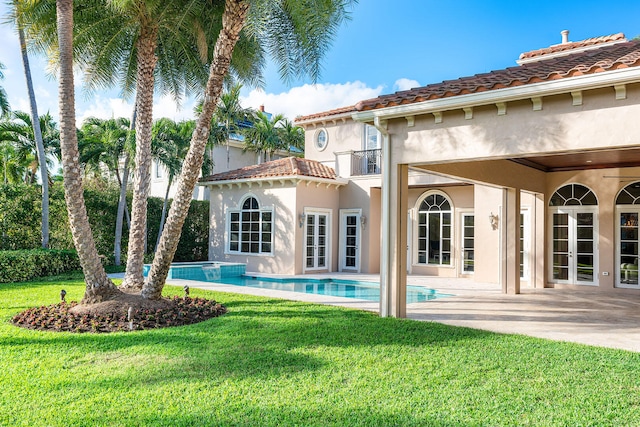 back of property with a yard, a balcony, a patio area, and a pool with hot tub