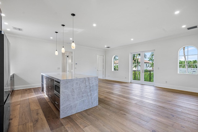 kitchen featuring a center island, hanging light fixtures, light hardwood / wood-style flooring, light stone countertops, and ornamental molding