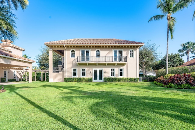 rear view of house featuring a balcony, a yard, and french doors