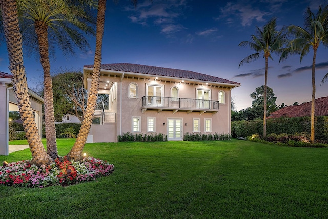 view of front of house featuring a lawn, a balcony, and french doors