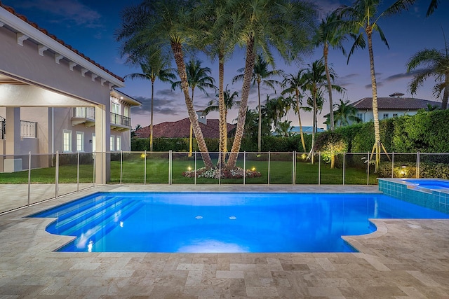 pool at dusk featuring a lawn and an in ground hot tub