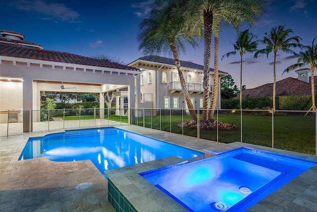 pool at dusk with an in ground hot tub, a yard, a patio, and ceiling fan