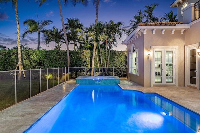 pool at dusk with an in ground hot tub, a patio, and french doors