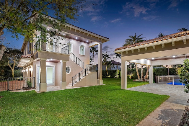 back house at dusk with a lawn, a patio area, and a balcony