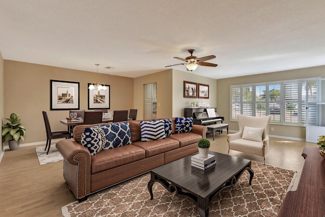 living room featuring light hardwood / wood-style floors, a textured ceiling, and ceiling fan with notable chandelier