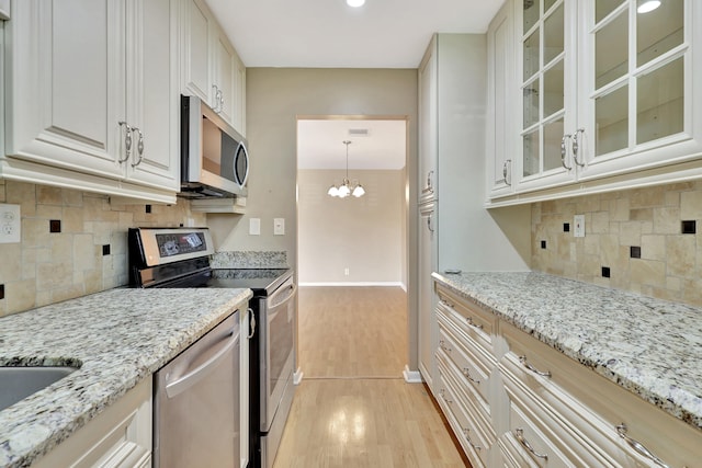 kitchen featuring appliances with stainless steel finishes, light hardwood / wood-style flooring, decorative backsplash, and an inviting chandelier