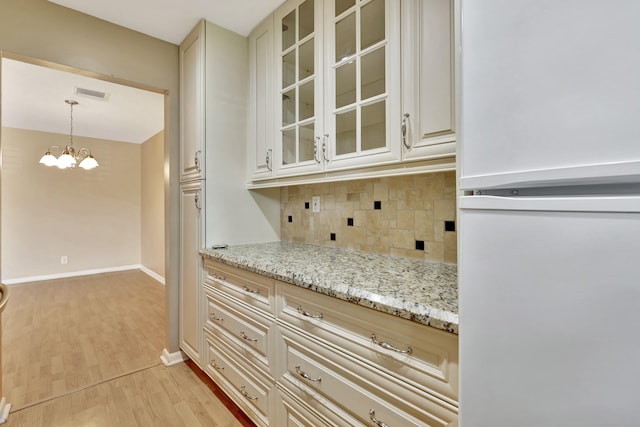 kitchen featuring light hardwood / wood-style flooring, backsplash, decorative light fixtures, a chandelier, and light stone counters