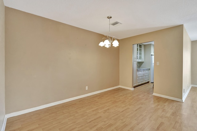 spare room with light hardwood / wood-style floors and a chandelier