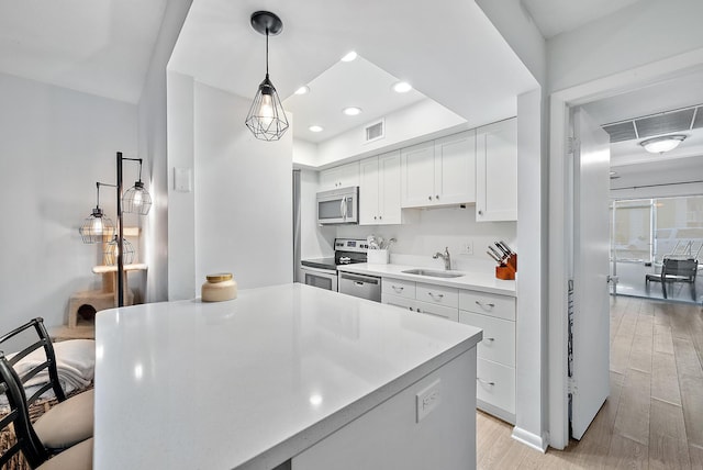 kitchen featuring white cabinetry, sink, hanging light fixtures, stainless steel appliances, and light wood-type flooring