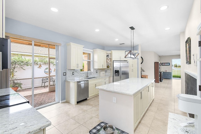 kitchen featuring stainless steel appliances, a center island, pendant lighting, light stone counters, and tasteful backsplash