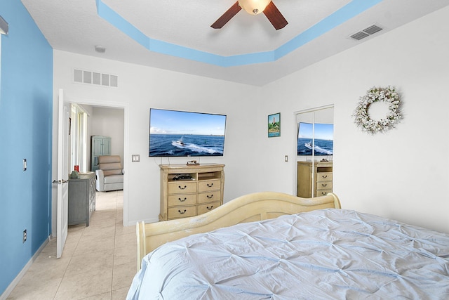 bedroom with light tile patterned flooring, a textured ceiling, a tray ceiling, and ceiling fan