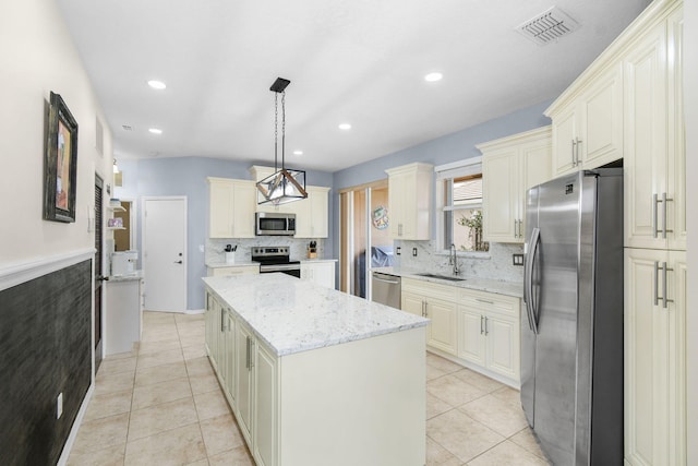 kitchen with appliances with stainless steel finishes, sink, a kitchen island, decorative light fixtures, and light stone counters