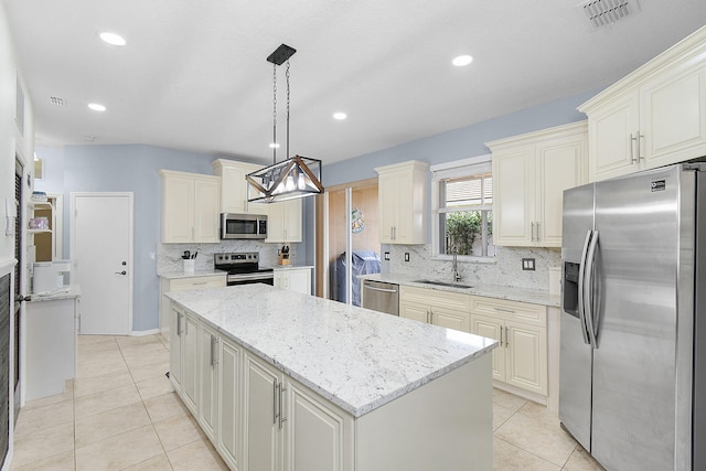 kitchen featuring appliances with stainless steel finishes, light stone countertops, sink, pendant lighting, and a center island