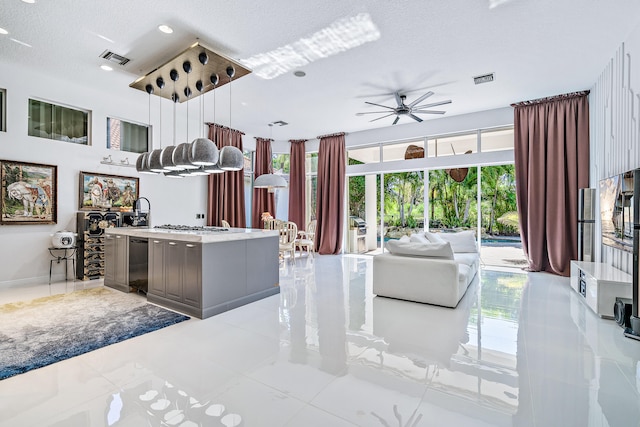 kitchen featuring an island with sink, ceiling fan, a textured ceiling, gray cabinets, and decorative light fixtures