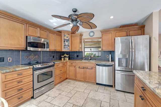 kitchen featuring backsplash, appliances with stainless steel finishes, ceiling fan, sink, and light stone counters