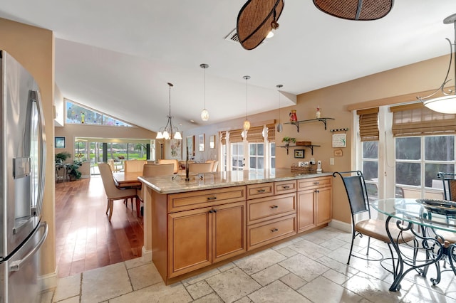 kitchen featuring lofted ceiling, stainless steel fridge, light stone counters, light wood-type flooring, and decorative light fixtures