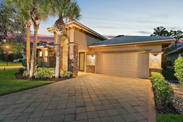 mediterranean / spanish home featuring stucco siding, decorative driveway, a garage, and stone siding