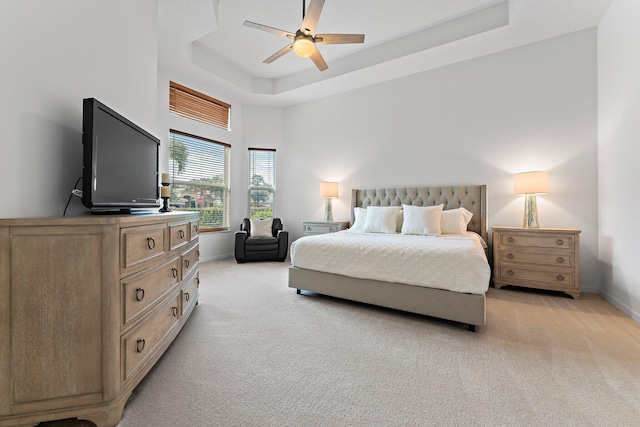 bedroom featuring a high ceiling, ceiling fan, a tray ceiling, and light colored carpet