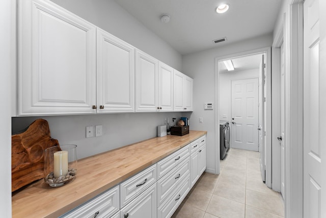 clothes washing area with cabinets, washer and dryer, and light tile patterned floors