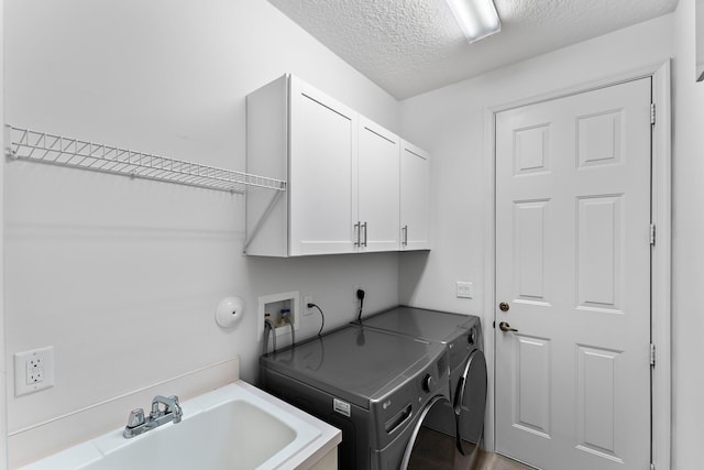 laundry area featuring wood-type flooring, sink, a textured ceiling, washing machine and clothes dryer, and cabinets