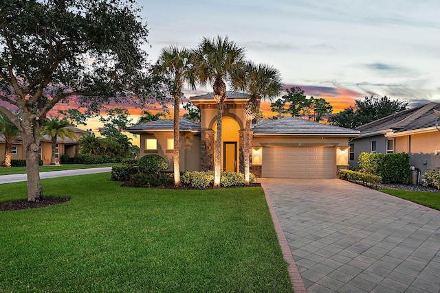 mediterranean / spanish home with stucco siding, decorative driveway, a garage, stone siding, and a lawn