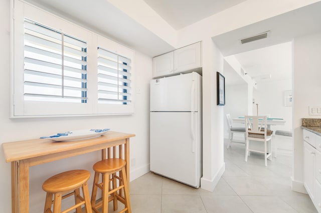 kitchen featuring light tile patterned floors, white cabinets, a breakfast bar area, and white fridge