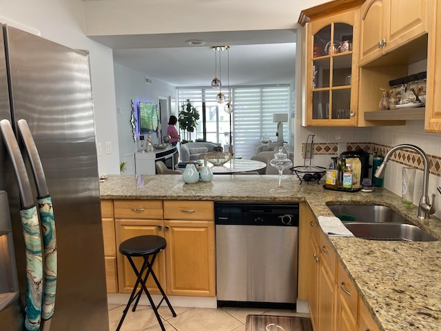 kitchen with hanging light fixtures, stainless steel appliances, sink, light stone countertops, and tasteful backsplash