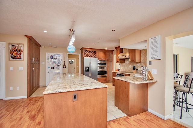 kitchen with custom exhaust hood, light stone counters, stainless steel appliances, and light wood-type flooring