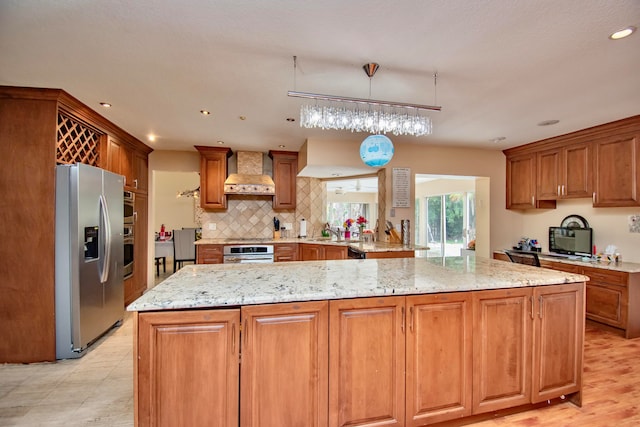 kitchen featuring kitchen peninsula, light stone counters, wall chimney exhaust hood, stainless steel refrigerator with ice dispenser, and decorative light fixtures