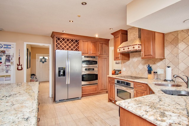 kitchen featuring decorative backsplash, sink, light stone countertops, custom exhaust hood, and appliances with stainless steel finishes