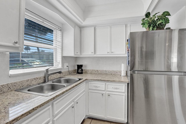 kitchen with sink, stainless steel refrigerator, light stone counters, ornamental molding, and white cabinets