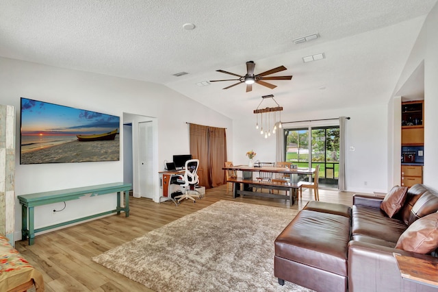 living room with ceiling fan with notable chandelier, a textured ceiling, light hardwood / wood-style flooring, and lofted ceiling