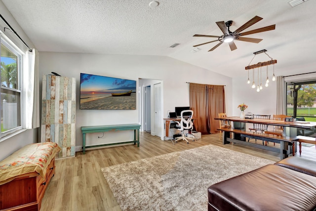 living room featuring ceiling fan with notable chandelier, a textured ceiling, light wood-type flooring, and lofted ceiling