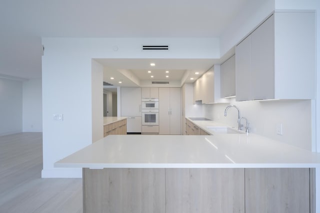 kitchen featuring double oven, black electric stovetop, kitchen peninsula, sink, and a raised ceiling