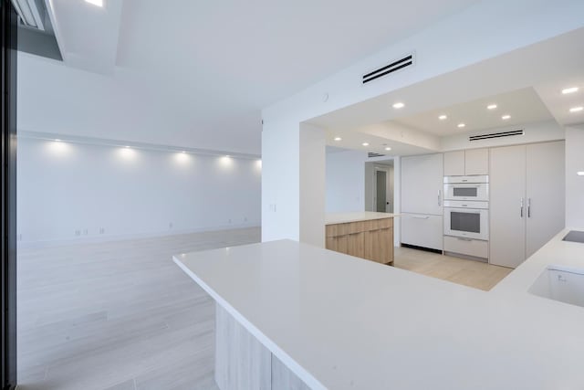 kitchen with a kitchen island, double oven, light hardwood / wood-style flooring, and white cabinets