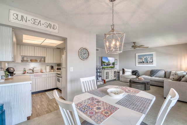 carpeted dining room featuring ceiling fan with notable chandelier, sink, and a textured ceiling