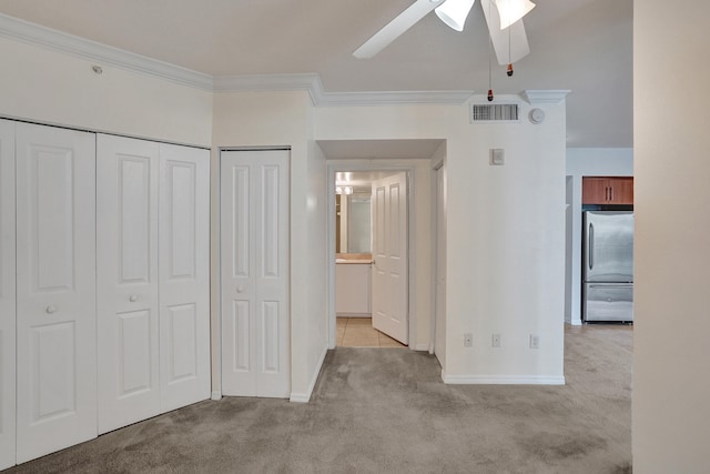 unfurnished bedroom with multiple closets, light carpet, crown molding, stainless steel refrigerator, and ceiling fan