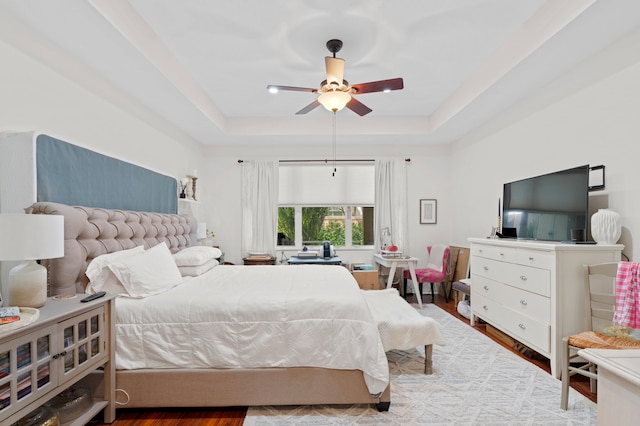 bedroom with hardwood / wood-style flooring, ceiling fan, and a raised ceiling