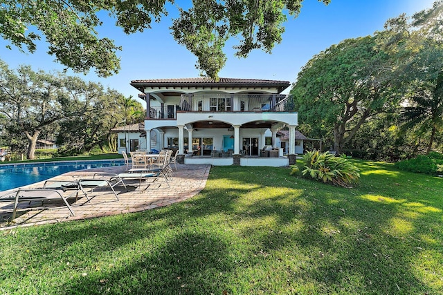 rear view of property with a balcony, a patio area, and a lawn