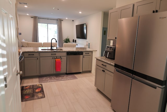 kitchen with light stone countertops, sink, light hardwood / wood-style flooring, and stainless steel appliances