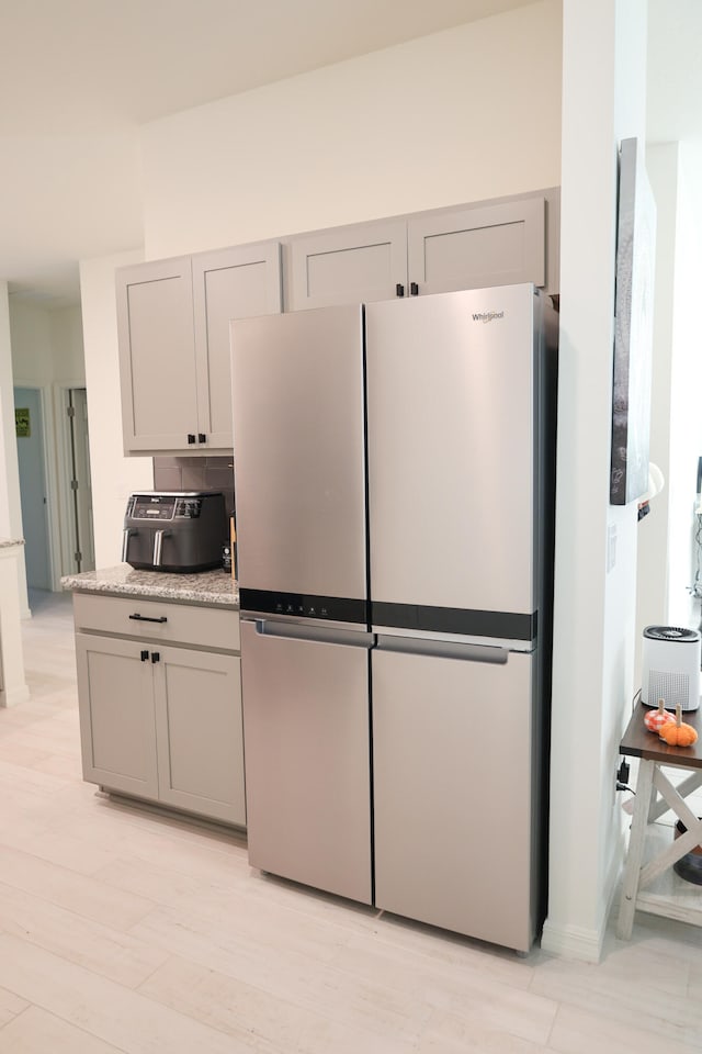 kitchen with gray cabinets, light hardwood / wood-style flooring, decorative backsplash, and stainless steel refrigerator