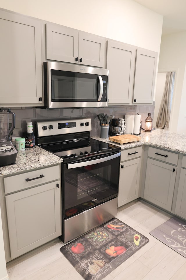 kitchen featuring backsplash, stainless steel appliances, light stone countertops, and gray cabinets