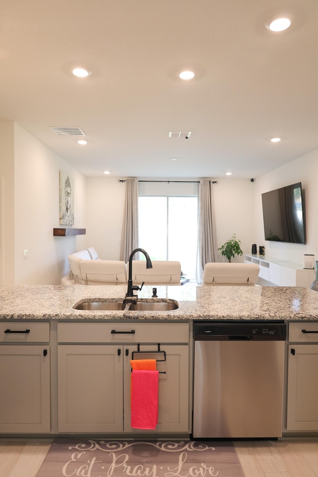 kitchen with stainless steel dishwasher, sink, light stone counters, and light hardwood / wood-style floors