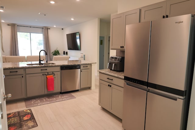 kitchen with sink, light stone countertops, stainless steel appliances, and light wood-type flooring