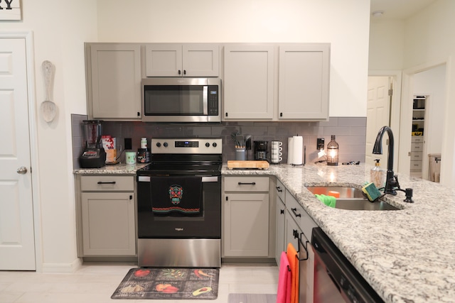 kitchen featuring sink, stainless steel appliances, gray cabinets, light stone counters, and decorative backsplash