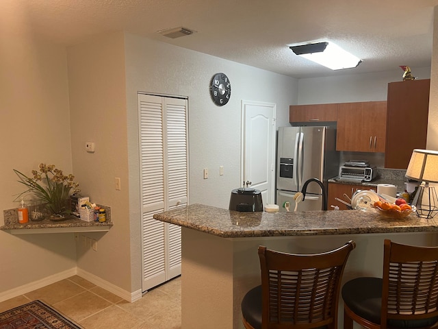 kitchen featuring a textured ceiling, kitchen peninsula, a kitchen breakfast bar, and stainless steel fridge