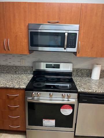 136 SW Peacock Blvd Unit 19-204, Port Saint Lucie, FL 34986 - kitchen featuring stainless steel appliances, tasteful backsplash, brown cabinetry, and light stone counters
