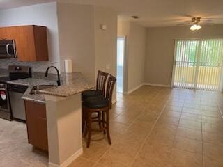 kitchen with kitchen peninsula, light tile patterned floors, ceiling fan, a breakfast bar, and stainless steel appliances