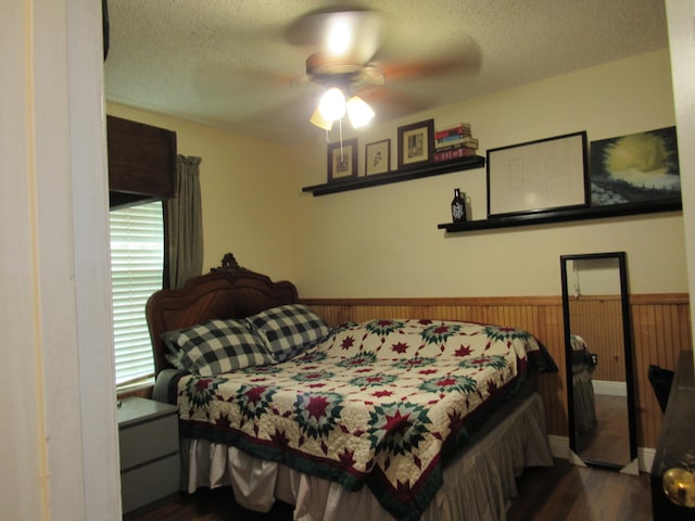 bedroom featuring ceiling fan, wood walls, a textured ceiling, and dark hardwood / wood-style floors